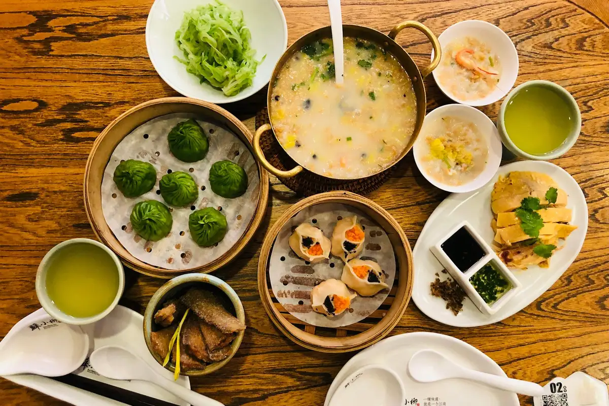 A table set for a dim sum feast, seen from above: steamers of shrimp dumplings, green dumplings, congee and cups of tea