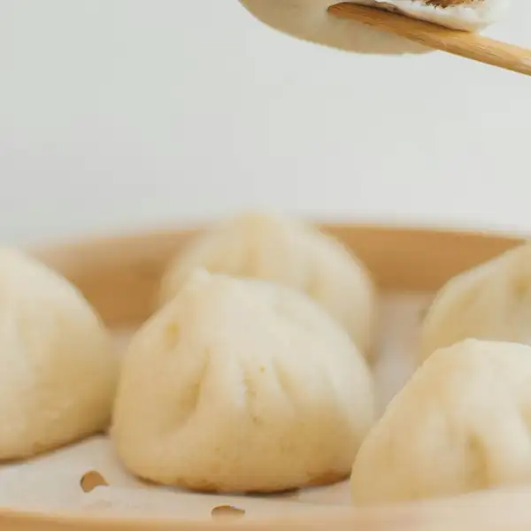 Soft white steamed buns side by side in a bamboo steamer