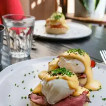 An eggs Benedict in daylight: poached egg, hollandaise and chives over peameal bacon on an English muffin
