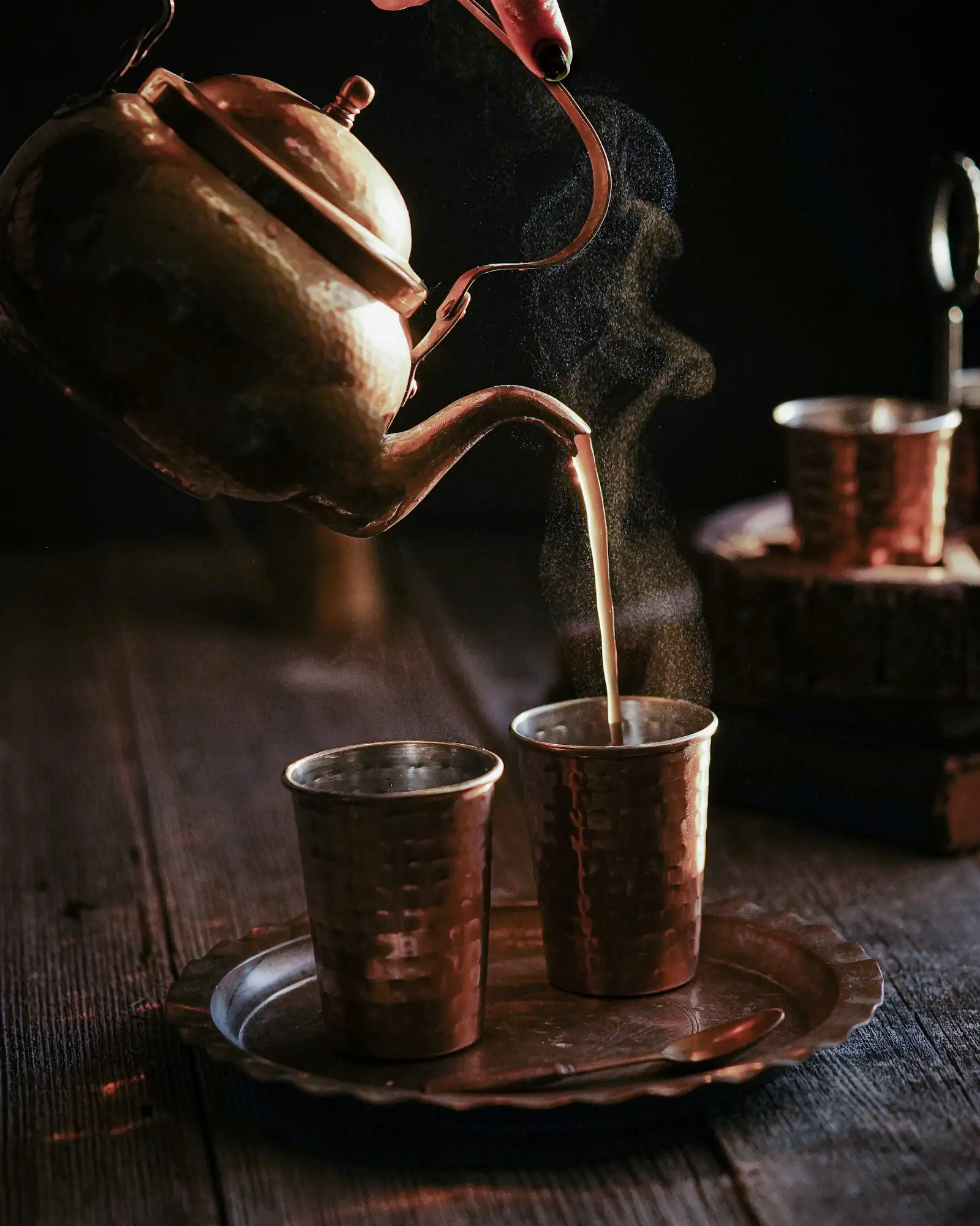 Masala chai poured from a copper kettle into two copper cups