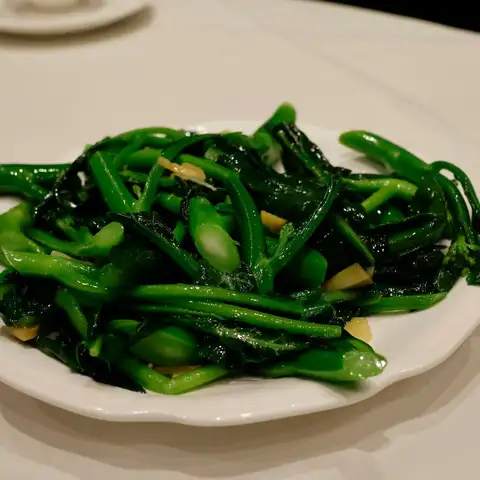 Bright green choy sum stir-fried with garlic on a white plate