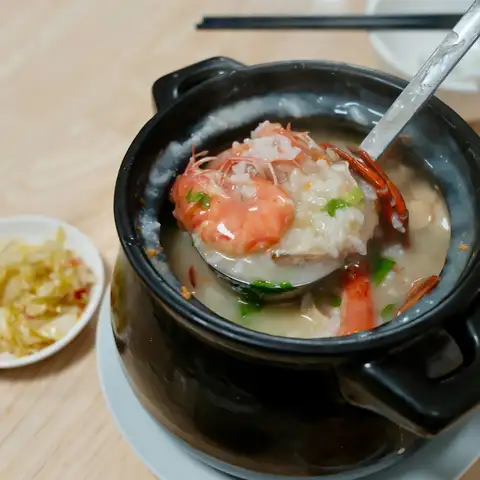 Seafood congee with shrimp in a black clay pot, a ladle resting in it