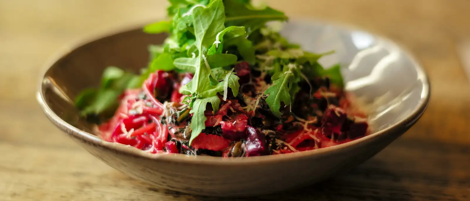 Shaved ember-roasted beet under bitter leaves in a stoneware bowl