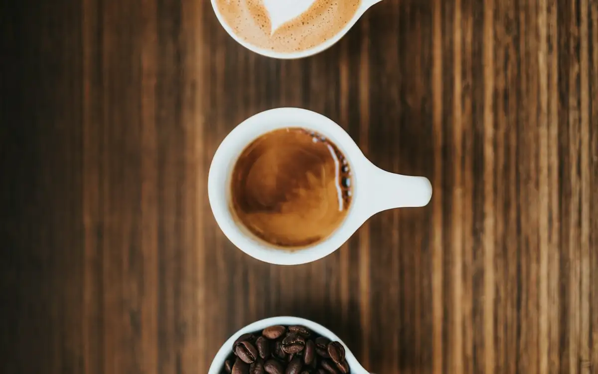Three cups in a row on dark wood: a latte, a cappuccino and a cup of whole beans