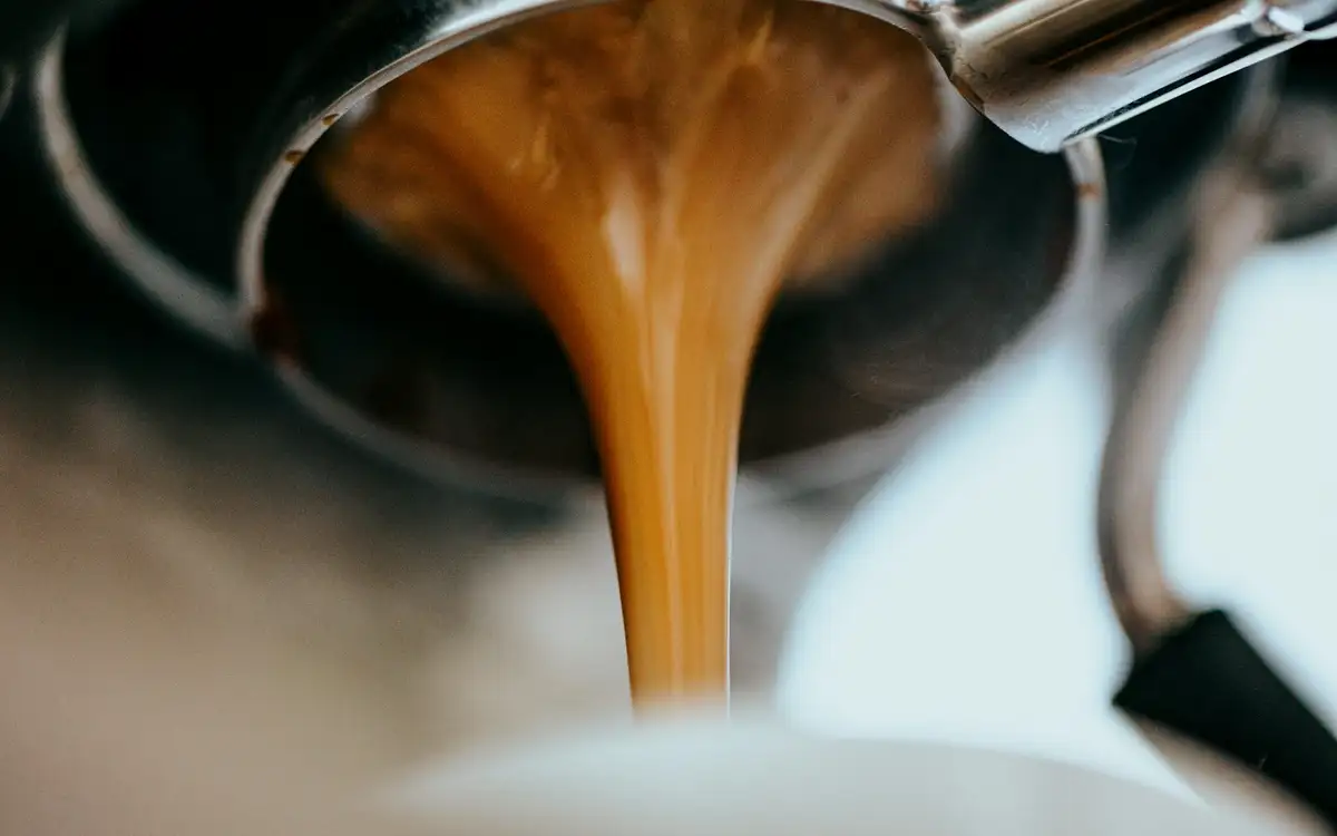 A double shot of espresso pouring from the portafilter in a thick caramel stream