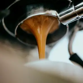 A double shot of espresso pouring from the portafilter in a thick caramel stream