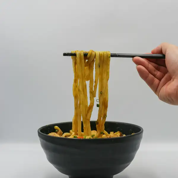 Chopsticks lifting noodles out of a black bowl