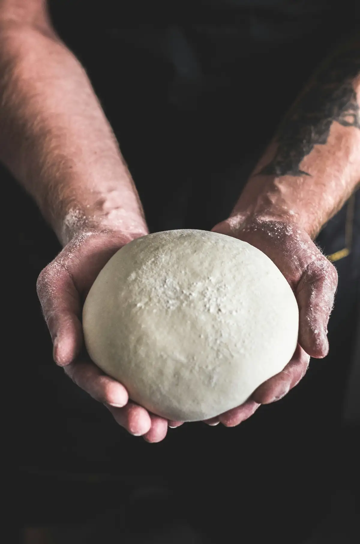 Floured hands holding a ball of pizza dough