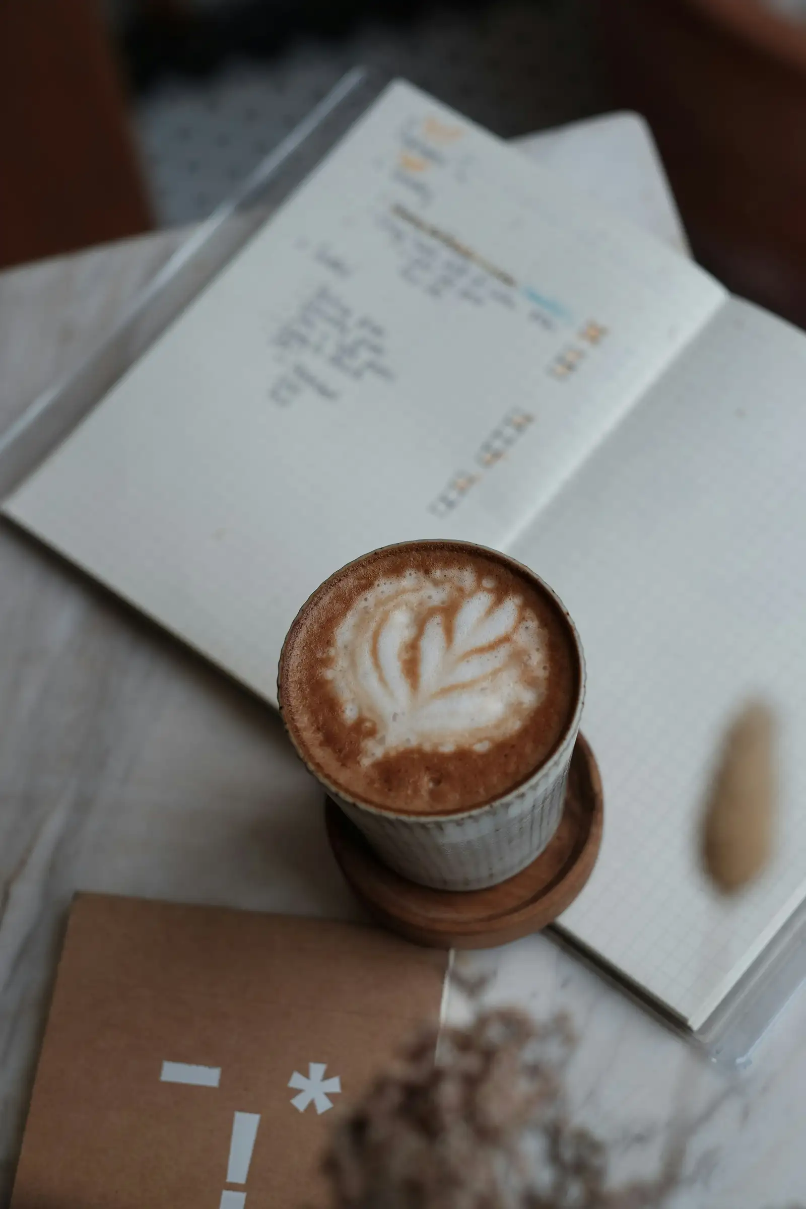 A latte with a leaf in the foam on an open notebook, from above