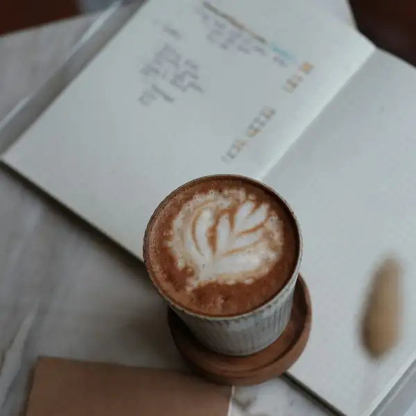 A latte with a leaf in the foam on an open notebook, from above