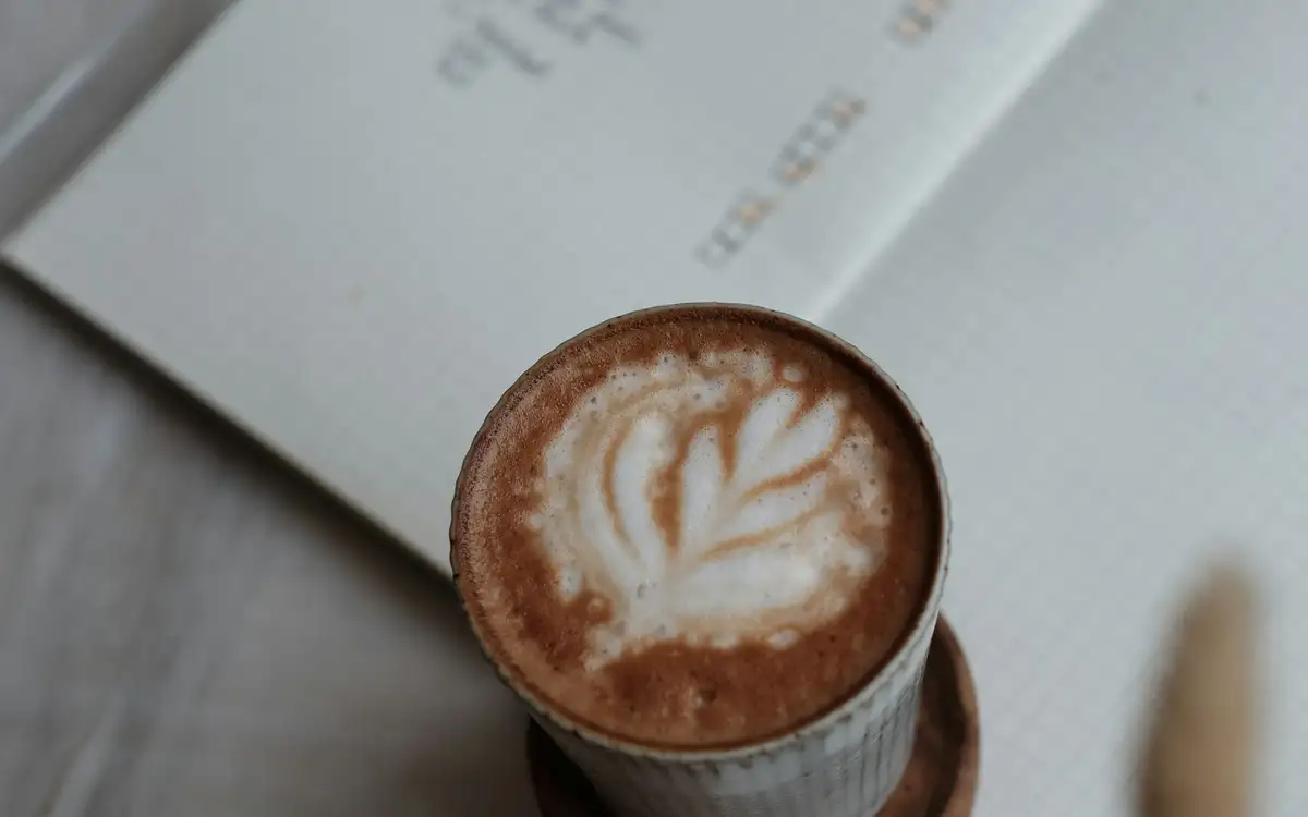 A latte with a leaf in the foam on an open notebook, from above