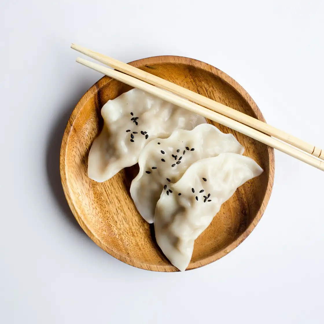 Three steamed dumplings in a round wooden basket, seen from above, chopsticks resting on the rim