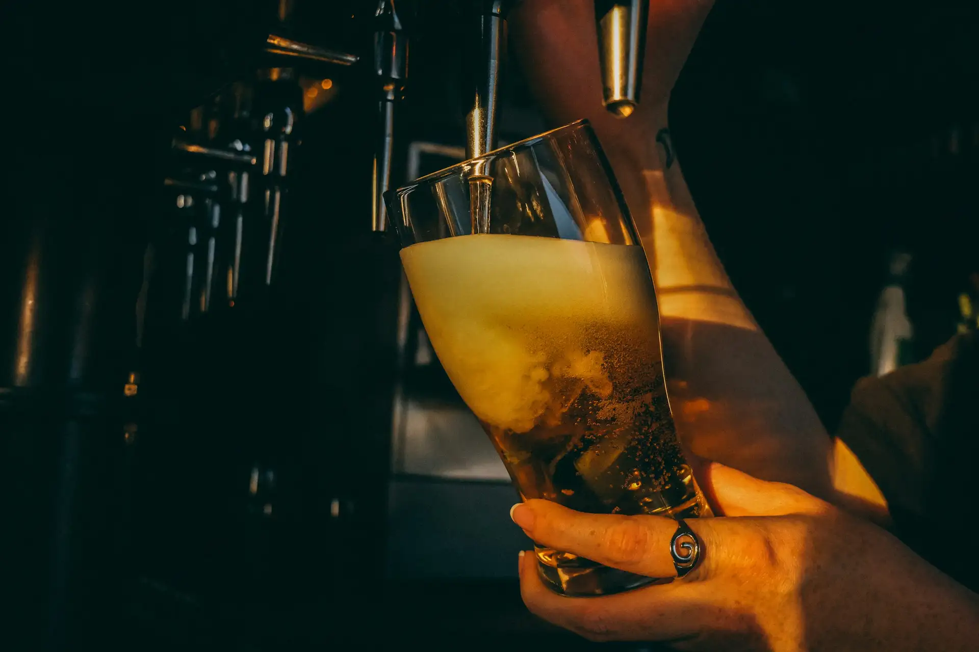 A pint of amber beer being poured from a tap in a dim bar