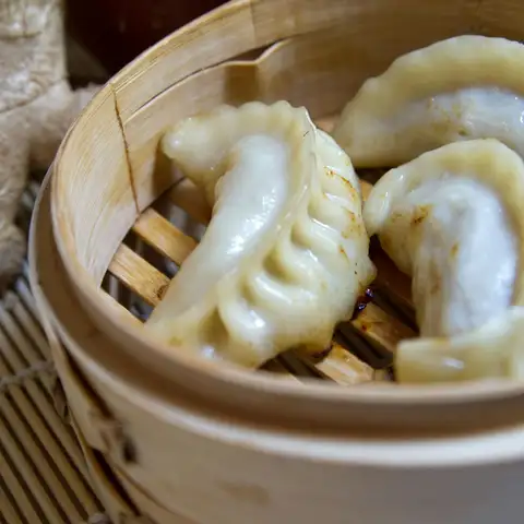 Pleated pork and chive dumplings in a bamboo steamer, a knob of fresh ginger beside it