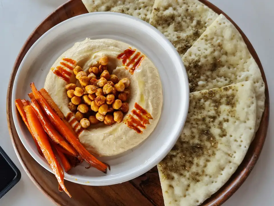 A swirl of hummus with whole chickpeas and paprika, carrots and warm pita on the side