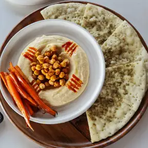 A swirl of hummus with whole chickpeas and paprika, carrots and warm pita on the side