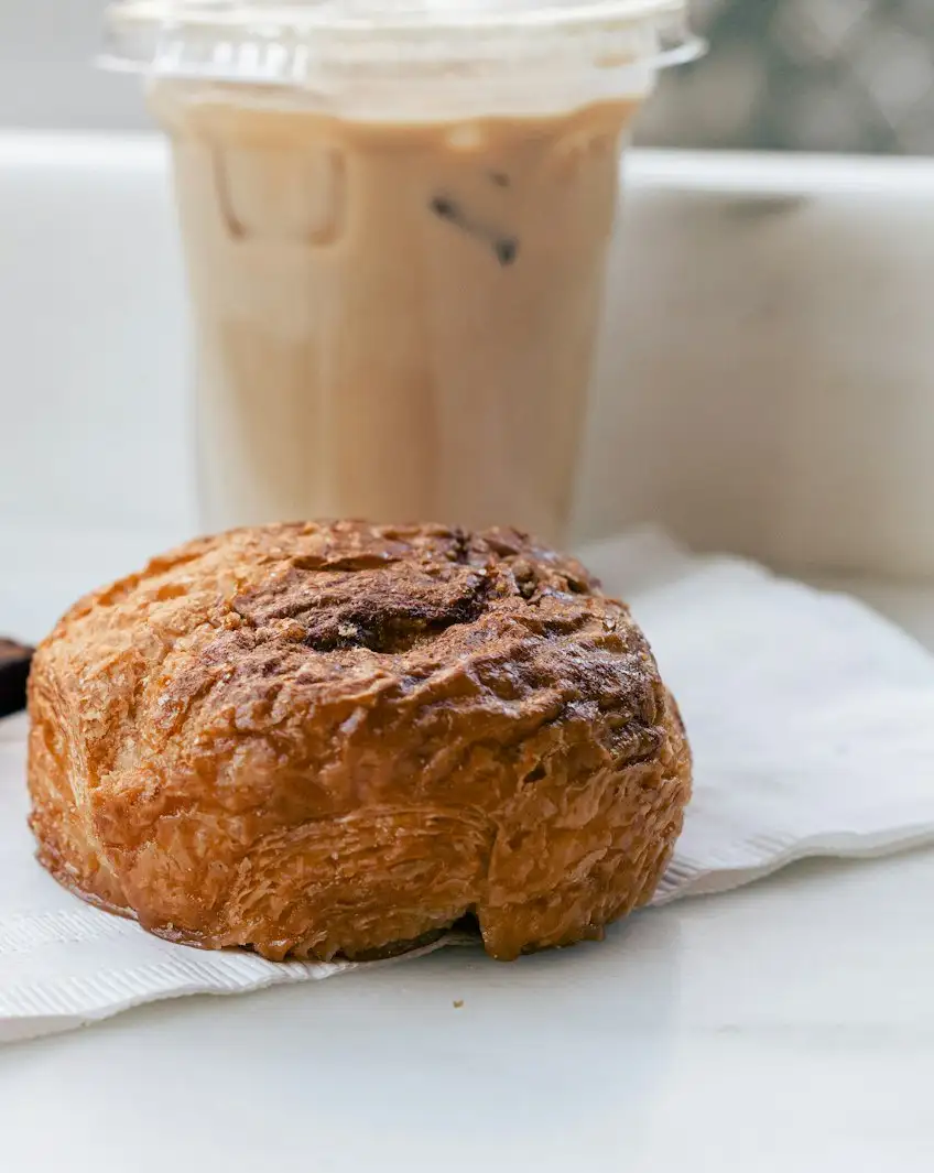 A round, deeply caramelised kouign-amann on a paper napkin beside an iced latte