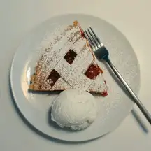 A slice of lattice-top pie dusted with sugar, with a scoop of vanilla ice cream and a fork