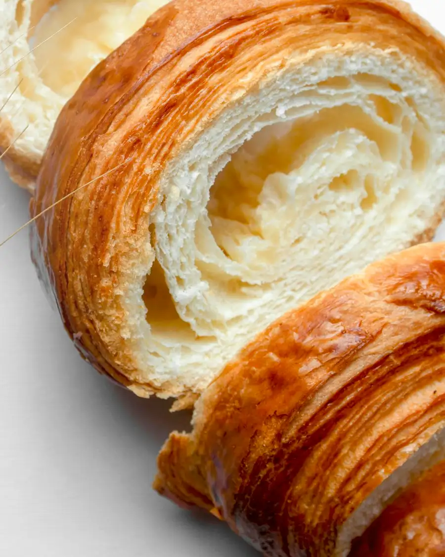 A croissant cut open to show its honeycomb crumb, beside stalks of wheat