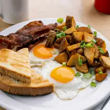 Two sunny-side-up eggs with bacon, toast and diced breakfast potatoes, black coffee alongside