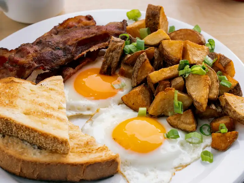 Two sunny-side-up eggs with bacon, toast and diced breakfast potatoes, black coffee alongside