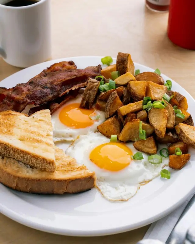 Two sunny-side-up eggs with bacon, toast and diced breakfast potatoes, black coffee alongside