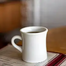 A white diner mug of coffee resting on an open menu at the counter