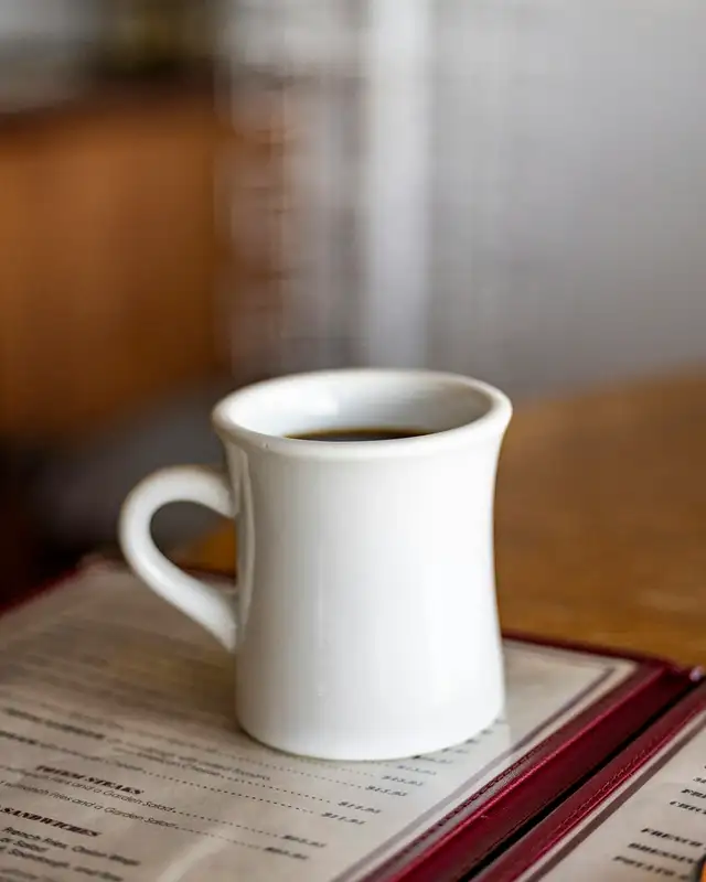 A white diner mug of coffee resting on an open menu at the counter