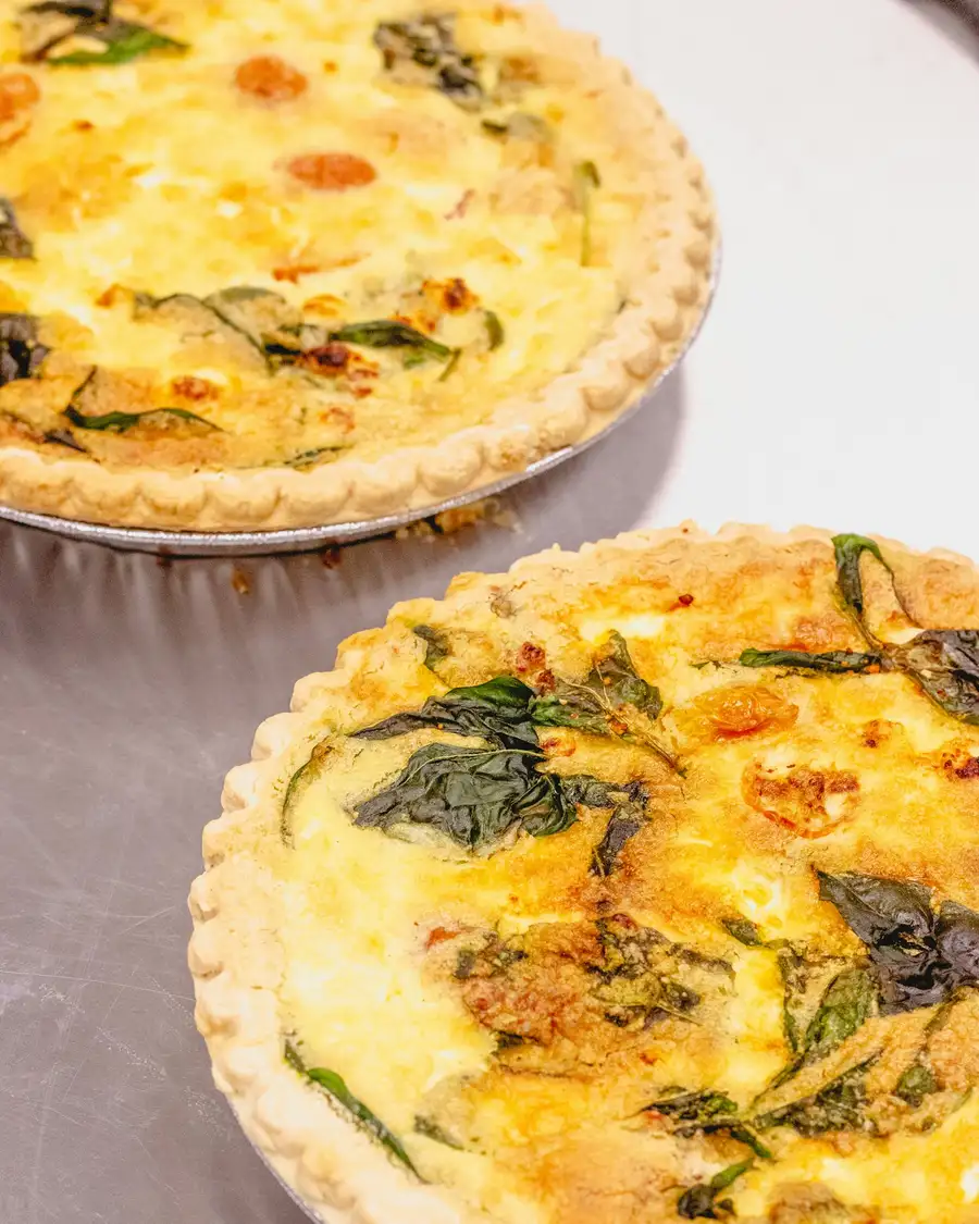 Two golden quiches flecked with leek and herbs, on a pale table