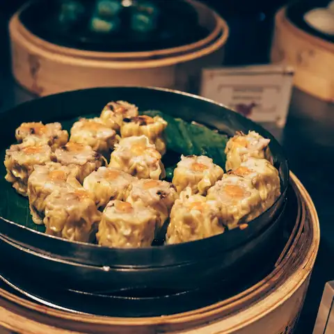 Siu mai with bright orange tops in a steamer basket, more bamboo steamers stacked behind