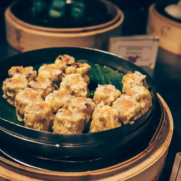 Siu mai with bright orange tops in a steamer basket, more bamboo steamers stacked behind