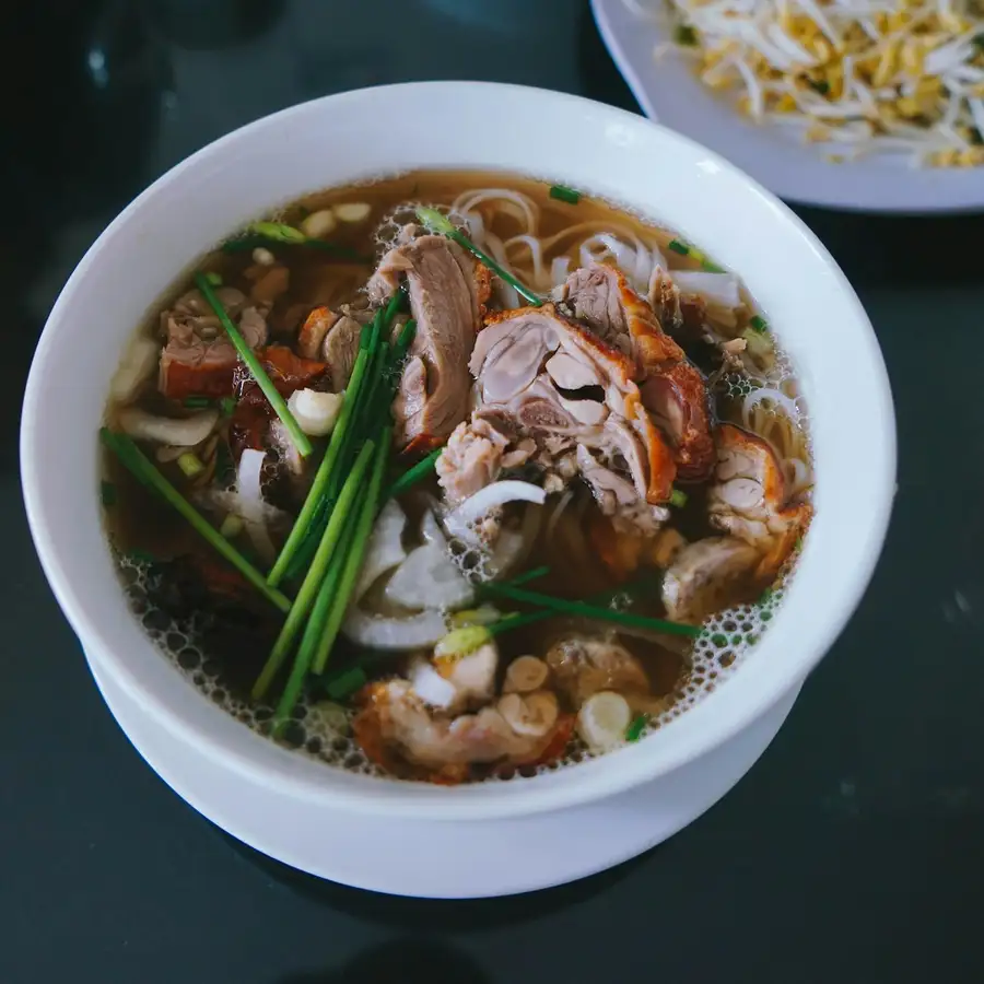 A white bowl of phở with sliced brisket, scallions and onion, bean sprouts on the side