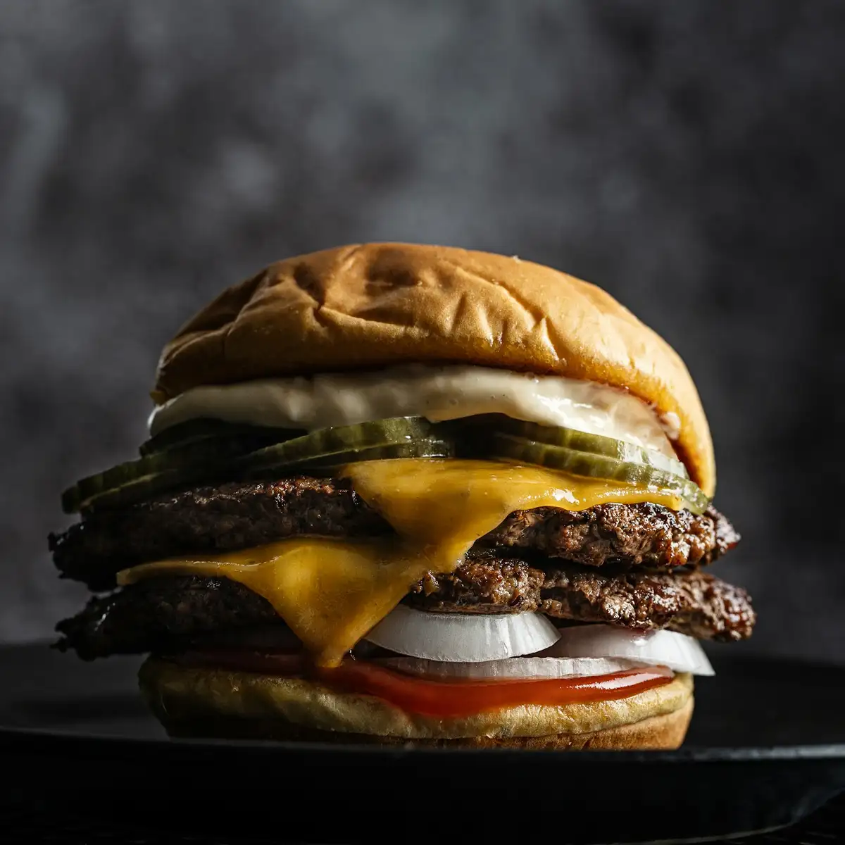 A double cheeseburger with melted cheddar and pickles on a dark board
