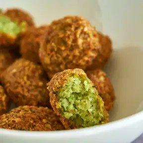 Falafel in a white bowl, two of them split open to show the bright green inside