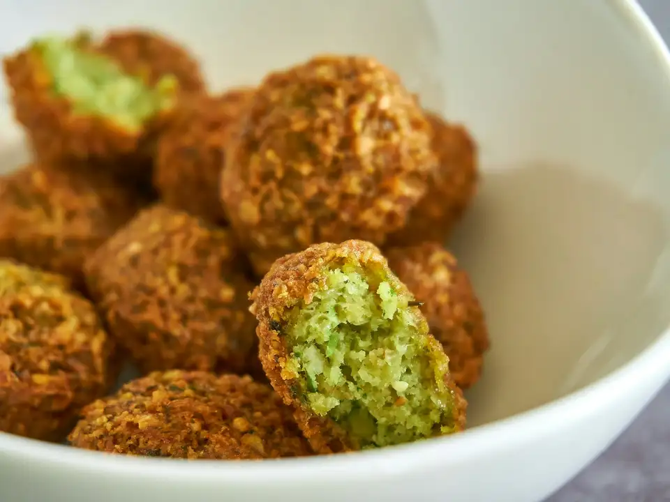 Falafel in a white bowl, two of them split open to show the bright green inside