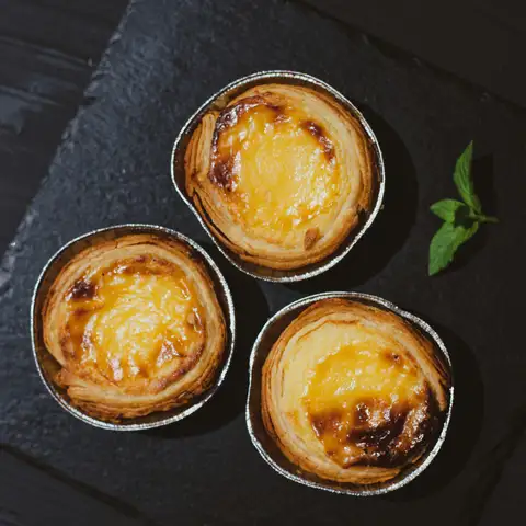 Three egg tarts with glossy golden custard on a slate board