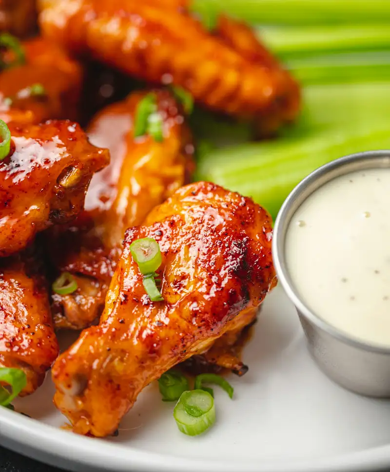 Glossy chicken wings with celery sticks and a cup of blue cheese dip