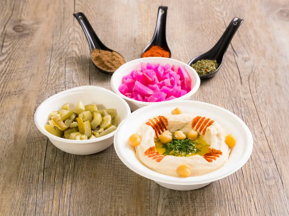 Bowls of hummus with olive oil and chickpeas, pickled turnip and green olives