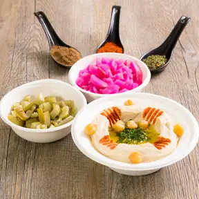 Bowls of hummus with olive oil and chickpeas, pickled turnip and green olives