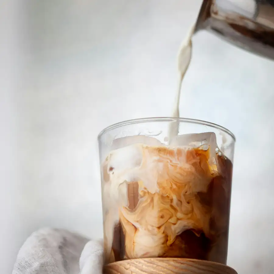 Milk poured over iced coffee in a short glass