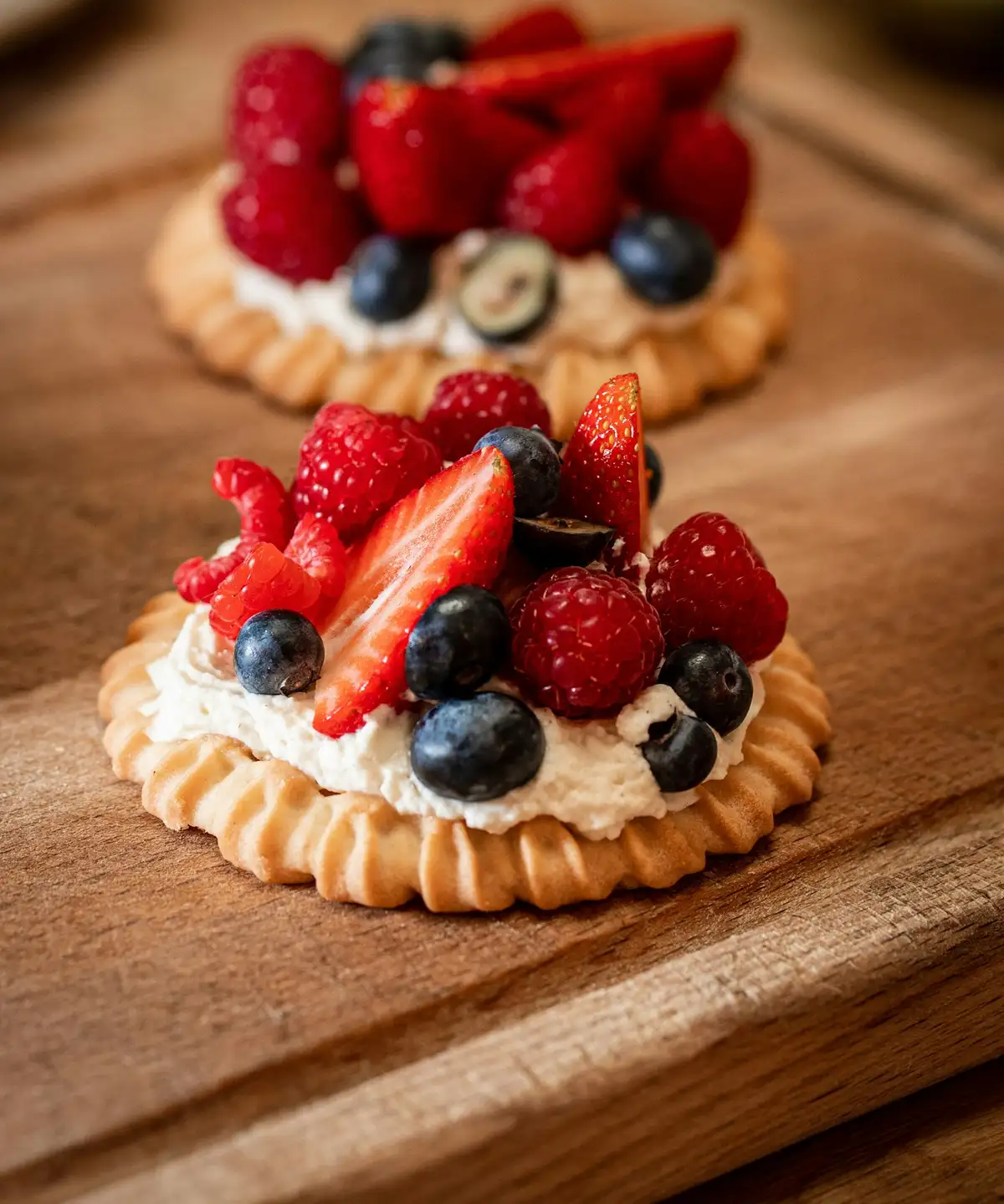 Two tartlets heaped with strawberries, raspberries and blueberries on a wooden board