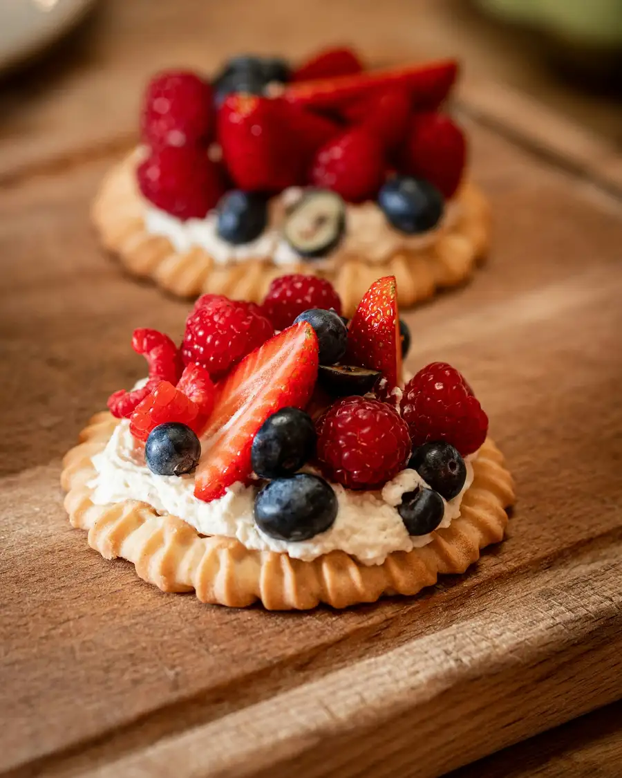 Two tartlets heaped with strawberries, raspberries and blueberries on a wooden board