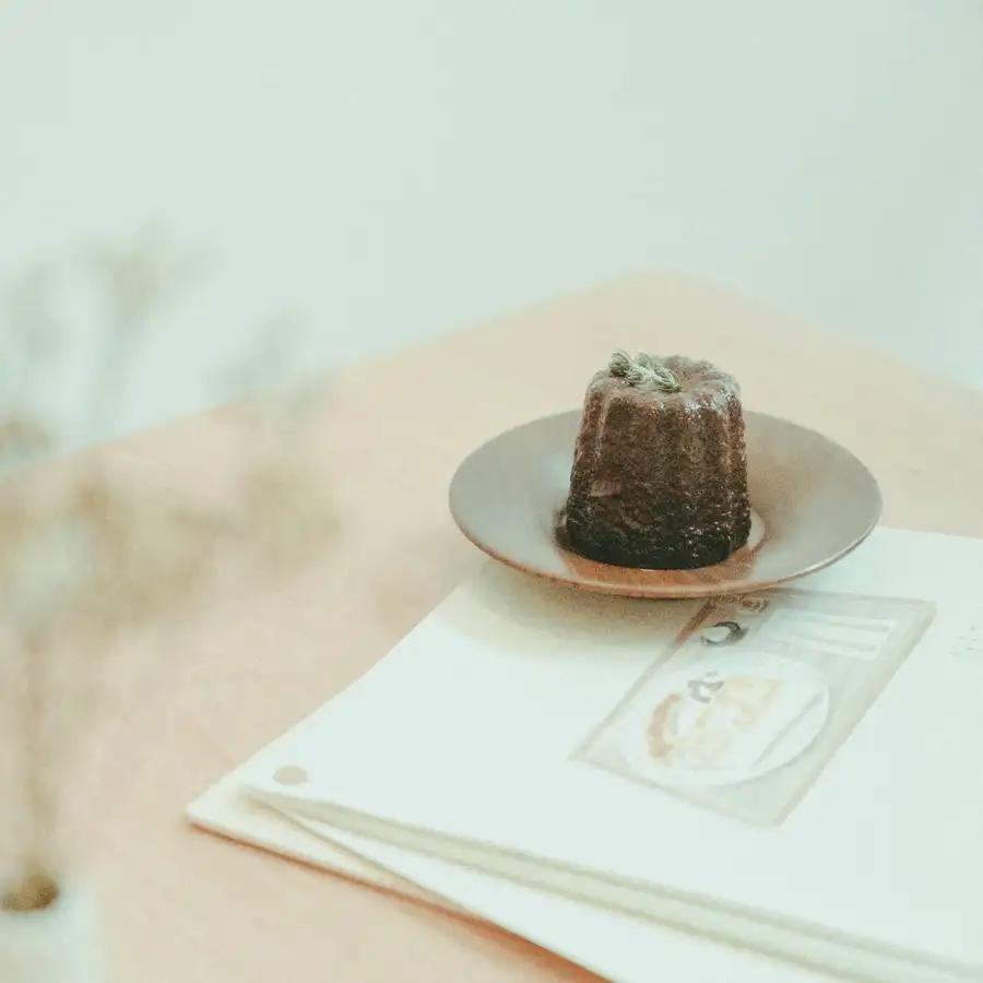 A dark, caramelised canelé on a small gold plate in soft morning light