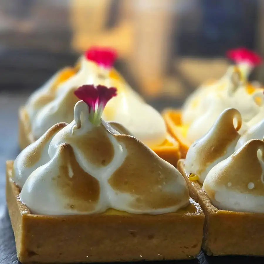 Square lemon tarts under peaks of torched meringue, each with a small red flower