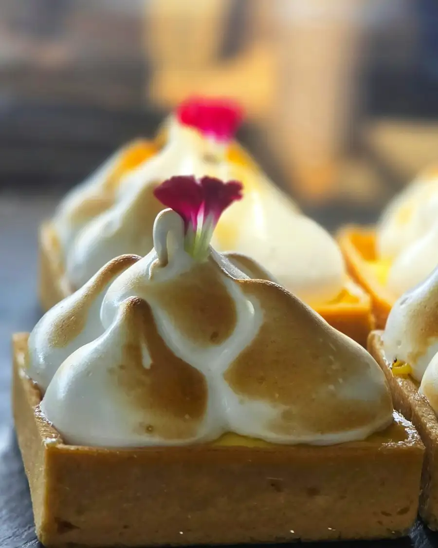 Square lemon tarts under peaks of torched meringue, each with a small red flower