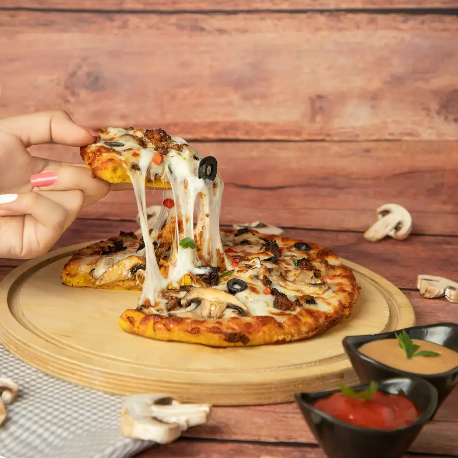 A slice lifted from a mushroom and olive pizza, the cheese stretching