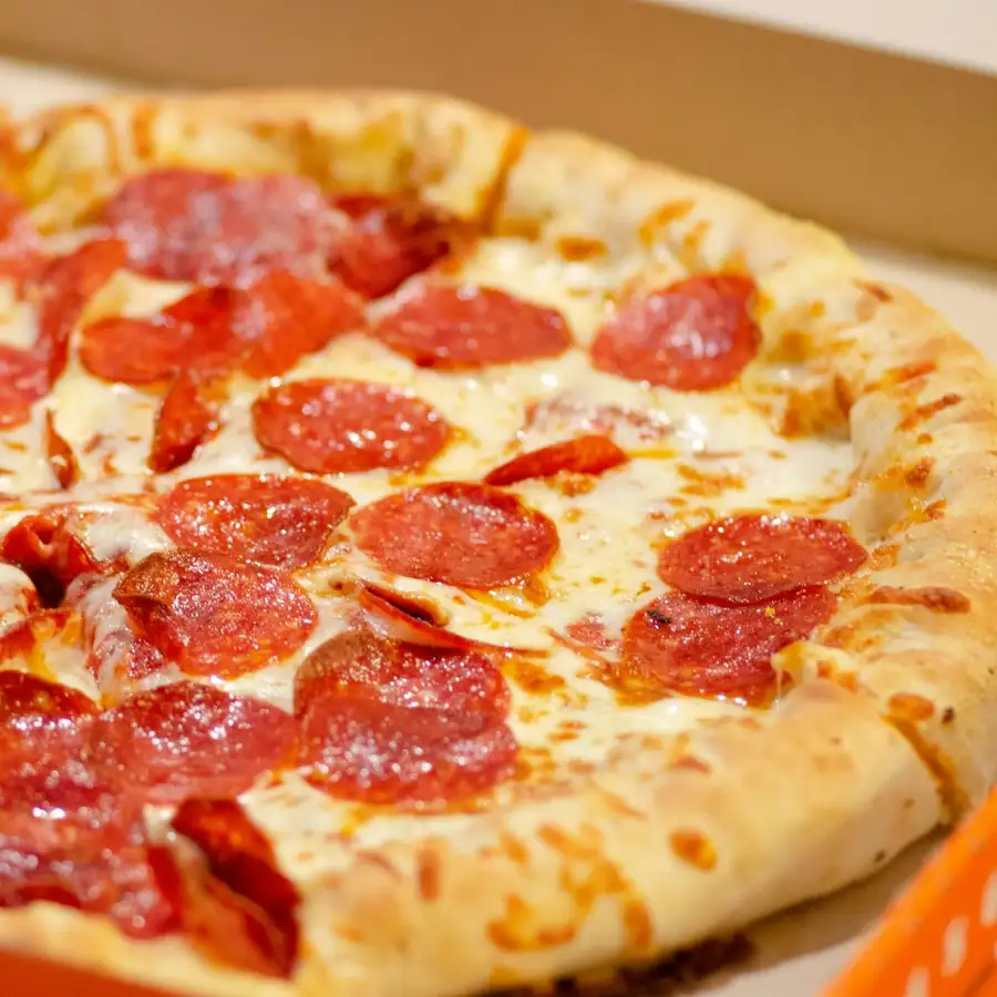 A pepperoni pizza in a takeout box, the slices edge to edge with pepperoni