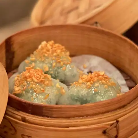 Crystal-skin dumplings flecked with green, topped with crisp golden garlic, in a bamboo steamer