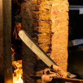 A shawarma spit glowing in front of the grill, its edges charred and crisp