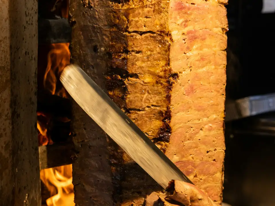 A shawarma spit glowing in front of the grill, its edges charred and crisp